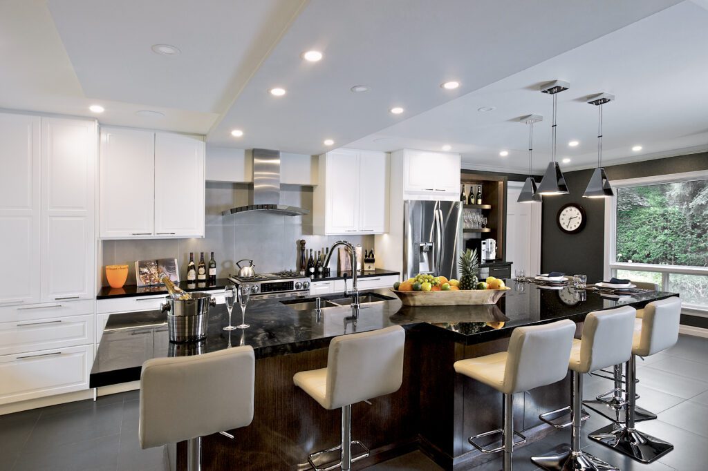 A kitchen with white shelves, black ceiling lamps, and gray chairs